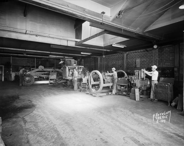 Interior of Nagle-Hart Tractor & Equipment Company with workmen and equipment, 754 East Washington Avenue. Large road grader in background.