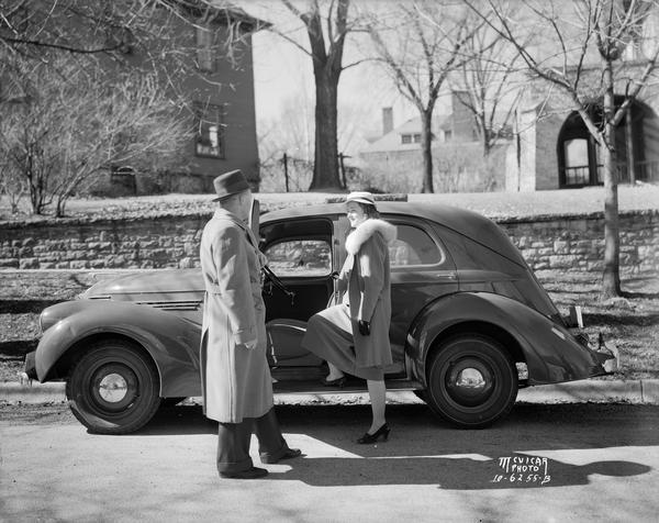 Mr. Smart from Smart Motors demonstrating a Willys automobile to a stylish woman, who has one foot up on the running board.