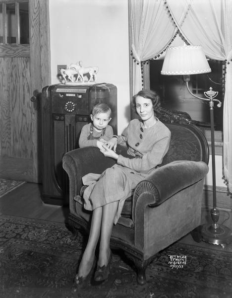 Portrait of Margaret (Mrs. Frank) Lewis sitting in a chair and Richard "Dickie" Lewis, a 3-year-old, standing beside the chair with floor model radio in the background.  Taken in the living room of Elwin Waste's house at 1321 Jenifer Street.