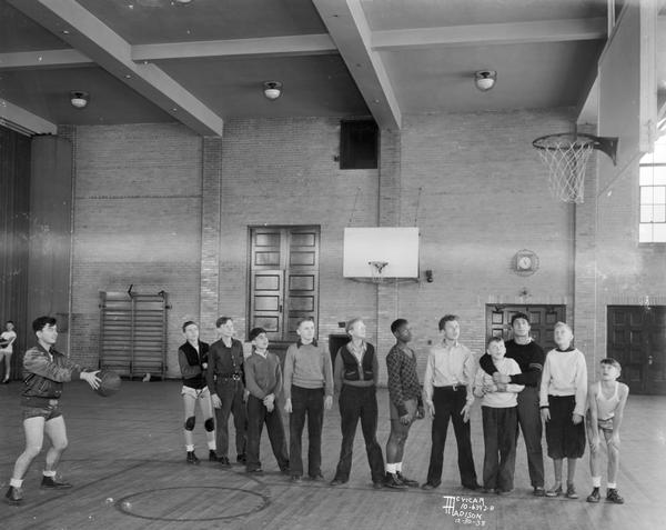 Eleven boys watching another practice a free throw for the Madison Department of Recreation boys basketball team.
