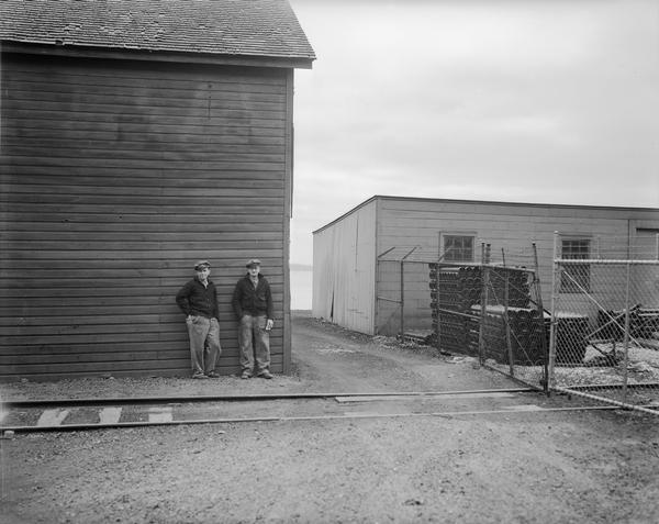 Two men standing against a wall, behind the Fauerbach Brewing Co. Railroad tracks are in the foreground, and Lake Monona is in the background.