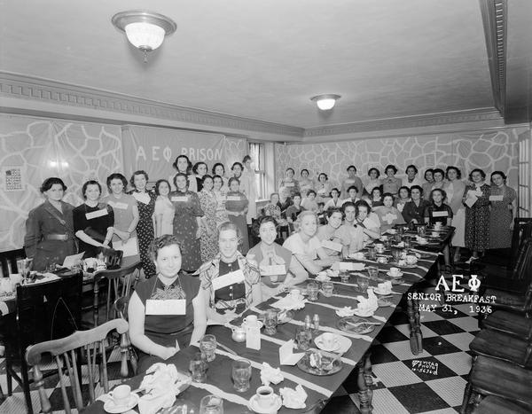 Group portrait of Alpha Epsilon Phi sorority members standing around banquet tables at senior breakfast, 22 Langdon Street.