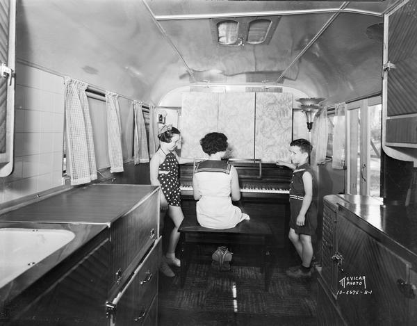 Interior view of Forbes Meagher trailer, with older child playing piano and two younger children watching.