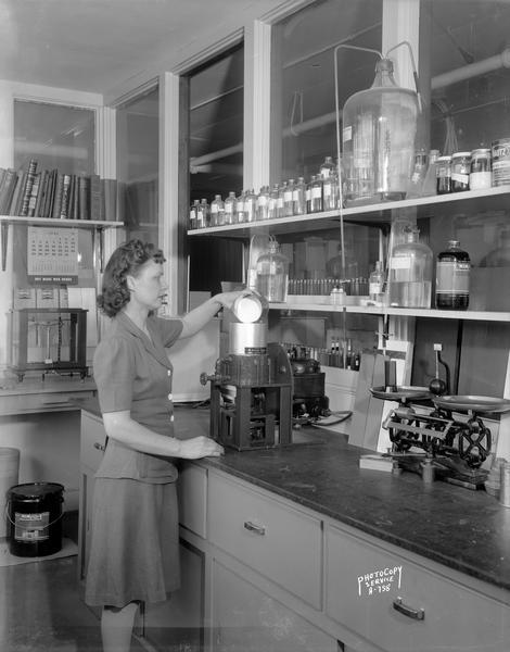 Female chemist using C.M. Ambrose Company paint mixer for testing paint at the Mautz Paint and Varnish Company, 939 East Washington Avenue.