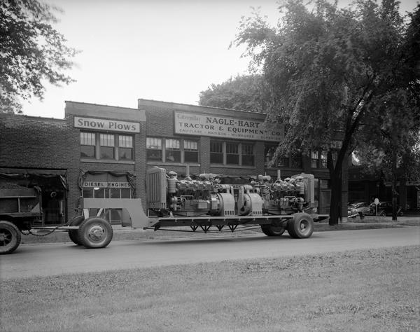 Two Caterpillar diesel electric engines Set 17-85 S on the back of a trailer truck parked in front of Nagle-Hart Tractor and Equipment Company, 754 East Washington Avenue.