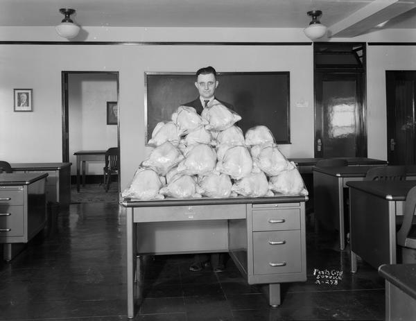 Man standing behind desk with fifteen dressed and wrapped turkeys stacked on top.