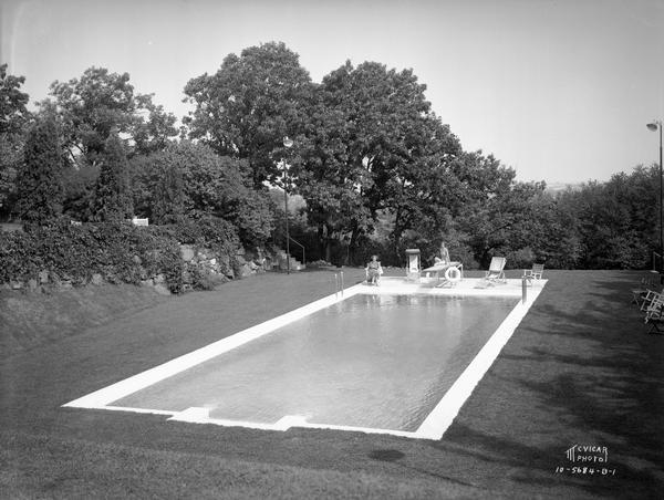 Dr. Frederick Davis residence, located at 6048 S. Highlands Avenue, also known as Edenfred. Two women are relaxing at the swimming pool. One woman is sitting on a chair, and the other woman is sitting on a diving board.