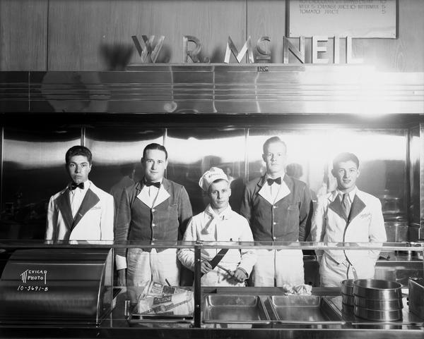 Group portrait of four waiters and one chef standing behind the counter at W.R. McNeil's Coffee Shop in the Park Hotel at 28 South Carroll Street.