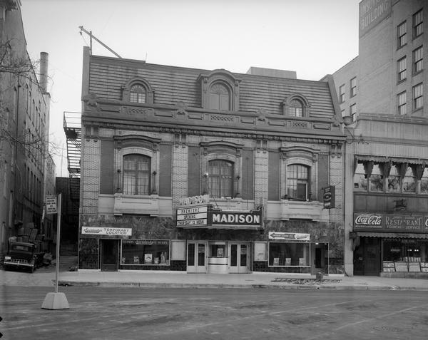 Front view of Madison Theatre, 111 Monona Avenue, with the Madison Theater building and Jimmy Dodge's restaurant. On the left is the temporary location of Savidusky's Cleaners and Dyers.