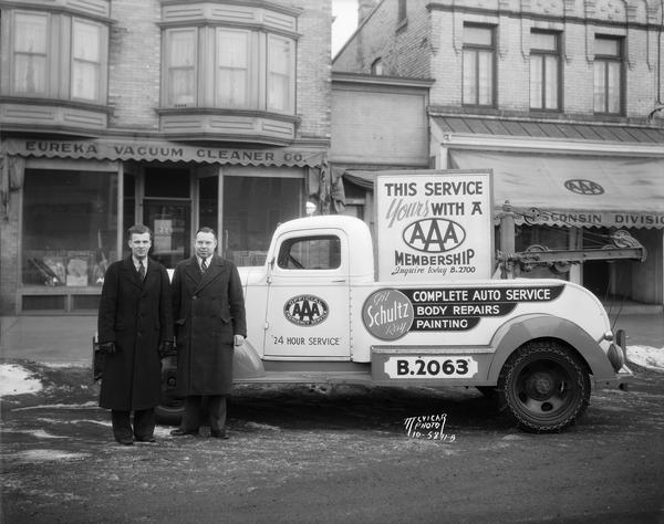 Benjamin Knotts and a representative of Schultz Tire and Battery Service, with a Schultz tow truck parked in front of the office of the Wisconsin Division of the American Automobile Association, 724 University Avenue, in Madison. Schultz provided the same type of emergency services enjoyed by AAA members today. Also behind the men is the Eureka Vacuum Cleaner Company.