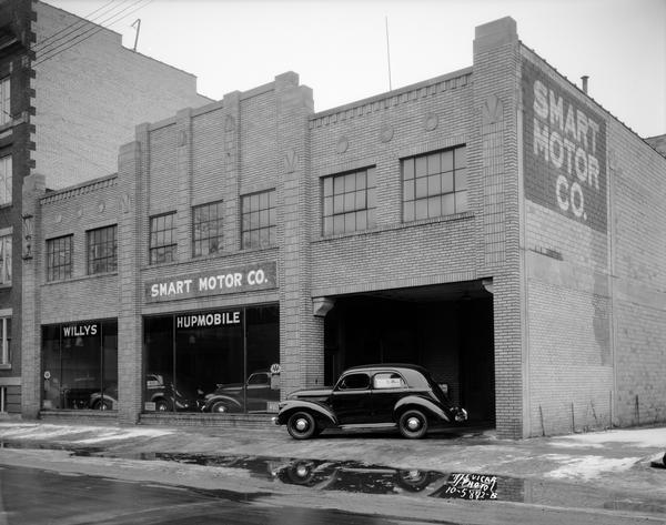 Willys car parked in front of Smart Motors, 437 W. Gilman Street. Signs in the show windows read: "Willys" and "Hupmobile."