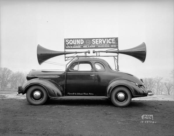 John P. Reed's Sound Service car with two loud speaker horns and a sign on top. The automobile is a Plymouth provided by Gillespie Blumer of Madison.
