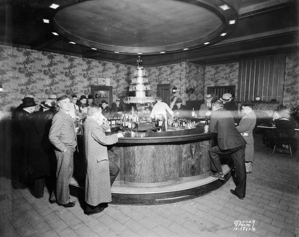 A group of men stand around the Circular Bar at the Park Hotel with two bartenders serving drinks.