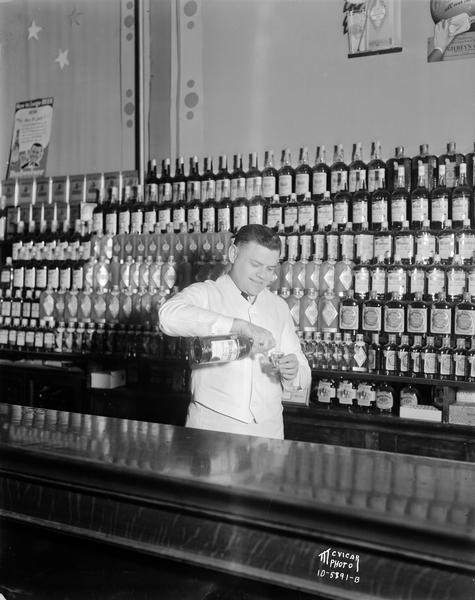 Albert Higgins pours whiskey behind the bar, backed by a large display of whiskey bottles in Camels Tavern, 619 University Avenue.