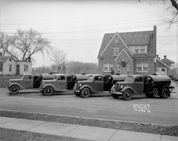 A fleet of four ton tank trucks (two each from Lafayette and Taylor counties) parked in front of Max Lehman's house, 1724 Park Street. The Warner house is on the left and a part of the graded school is visible behind the Lehman house.