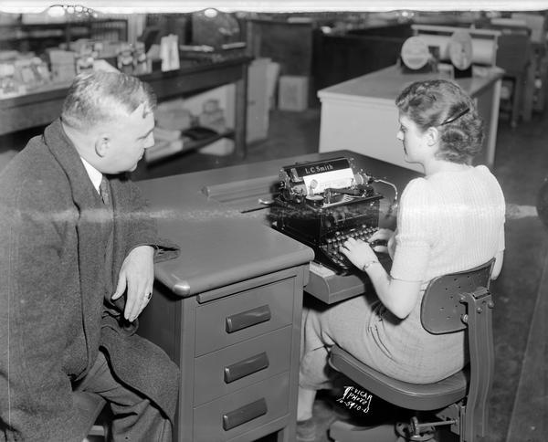 A man watching as a woman demonstrates typing on an L.C. Smith typewriter at Jones Typewriter Co., 506 State Street.