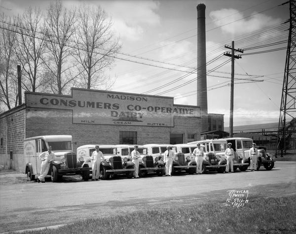 Seven milkmen standing beside dairy delivery trucks — all Internationals — parked in front of Madison Consumers Co-operative Dairy, 102 S. Dickinson Street.