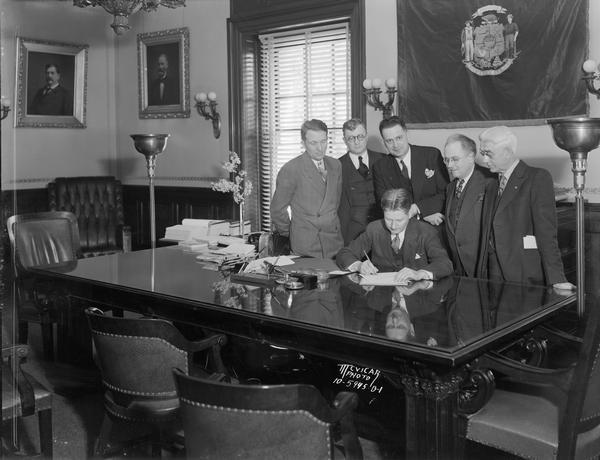 Governor Philip F. La Follette signing a bill in the Governor's office with onlookers.
