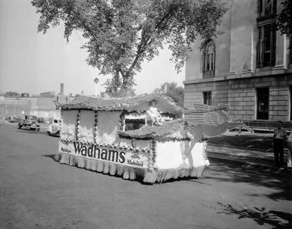 Wadhams Oil Company float in the Elks Parade, with a child "driving" a Mobile Oil Flying Red Horse symbol. The float is on E. Doty Street with the Post Office in the background.