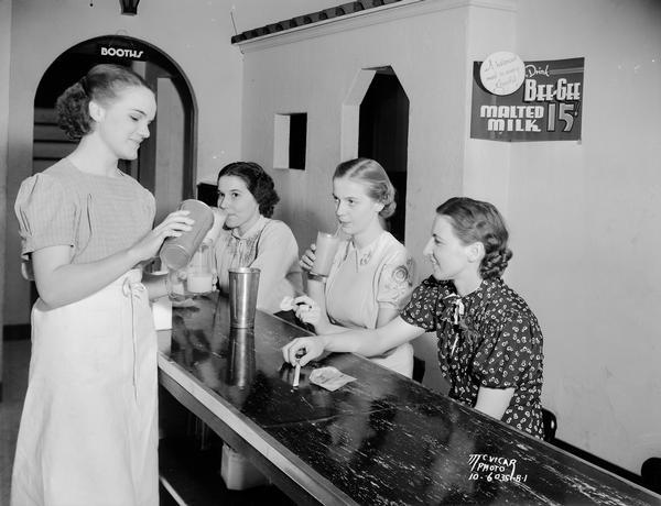 A soda jerk pouring a malt into a glass as three women are sitting at the counter of McCoy's Ice Cream Parlor, located at 507 State Street.
