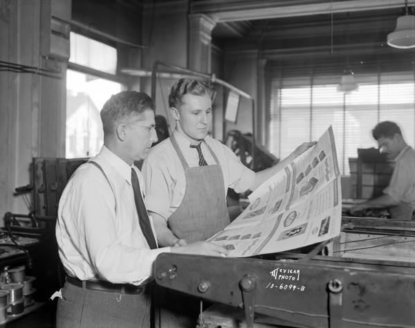 Herman Straus and son standing in front of printing press at Straus Printing Co., 214 East Washington Avenue.