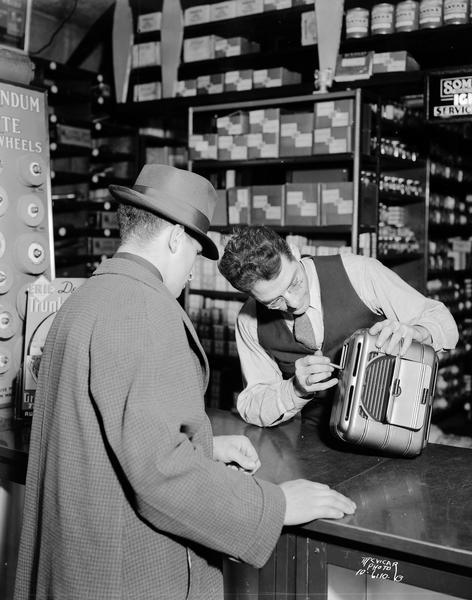 Man demonstrating automobile heater to a customer at Halperin Auto Parts, 209 South Park Street.