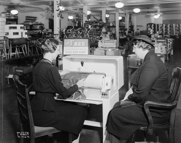 Sales woman demonstrating a Maytag Ironer (mangle) to a customer in the Burdick & Murray Department Store, located at 26-30 N. Carroll Street.