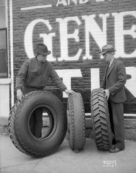 Two men comparing a large retreaded General tire against a worn out tire at a Diamond gas station. Monona Tire Co., 128 S. Pinckney Street.