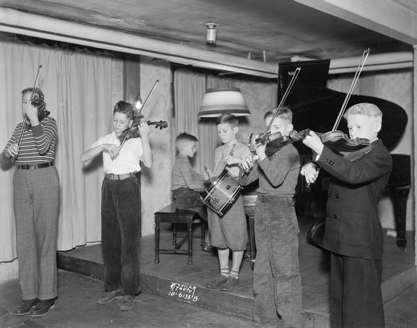 Six children playing violins, a drum and a piano at the Wisconsin School of Music.