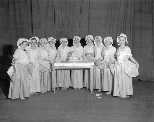 Girls dressed in colonial costumes are standing around a table with a birthday cake at the Emerson School P.T.A. 38th anniversary program.
