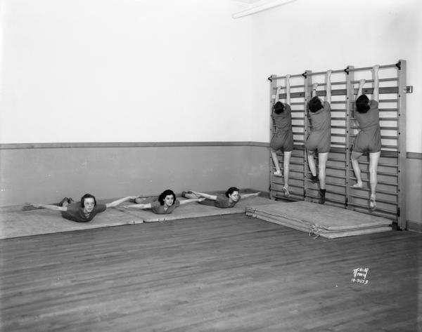 West High School girls in gym suits exercising on floor mat and climbing up exercise bars.