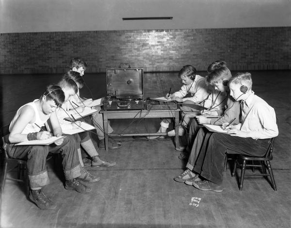 Boys at Emerson School are listening intently to earphones and writing on notebooks during a hearing test.