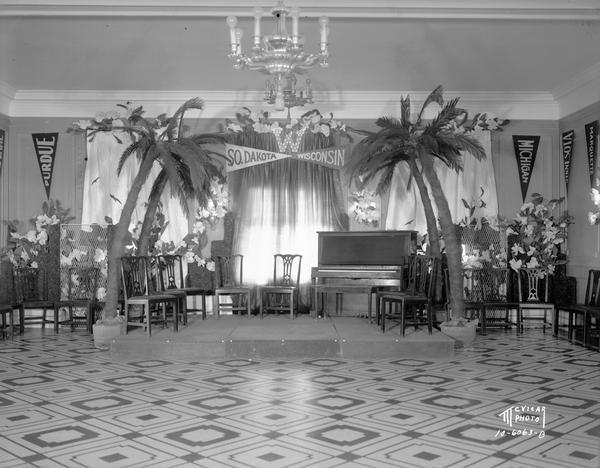 A bandstand and dance floor set up for a party at the Madison Club after the South Dakota vs. Wisconsin football game, with palm tree decorations.