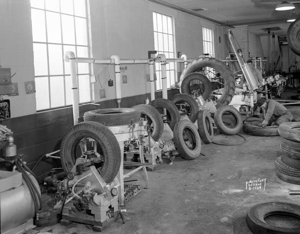 Interior of Holmes Tire and Supply Company, 431 West Main Street. View of the recapping department with two workers, equipment, and many tires of different sizes.