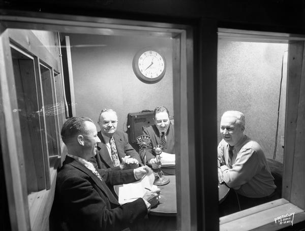 Four men sitting at a table around WIBA and WIBU radio microphones in the Oscar Mayer broadcast booth.