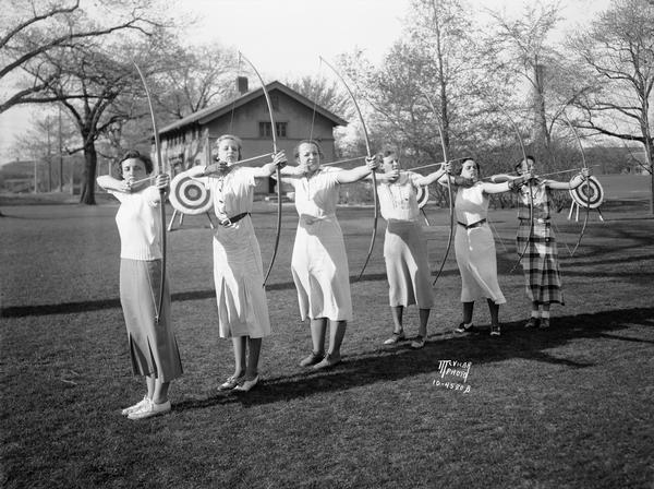 Six University of Wisconsin coeds, members of the Archery Club, posing on the archery field with bows drawn.