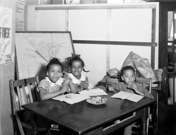 Three members of the Emerson Fresh Air school and the Longfellow Nutrition room eating at a table to demonstrate that the Kiddie Camp's provision of good nutrition will benefit "pre-tubercular" children.