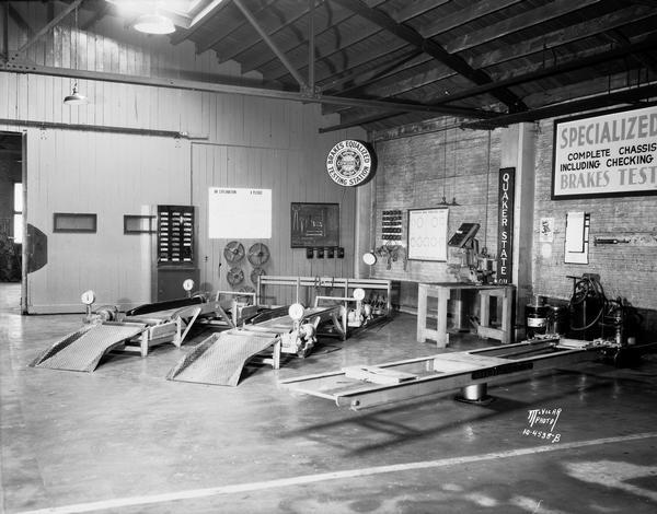 Interior of the J.A. Brady Garage, 1307 Williamson Street, with racks to elevate cars and the following signs: "Quaker State Oil" and "Cowdrey Brake Testing."