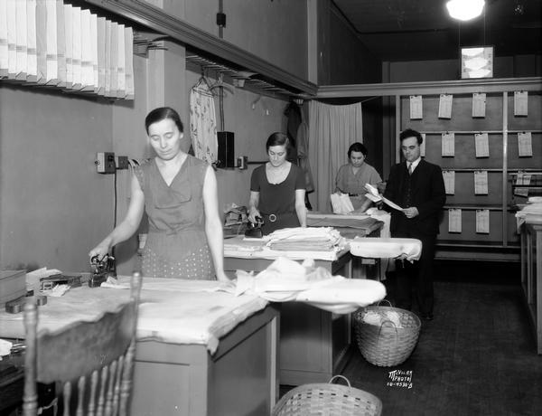 Interior of the Cardinal Hand Laundry, 619 State Street. Two women are ironing, while another woman is folding clothes while under the attention of their male supervisor.