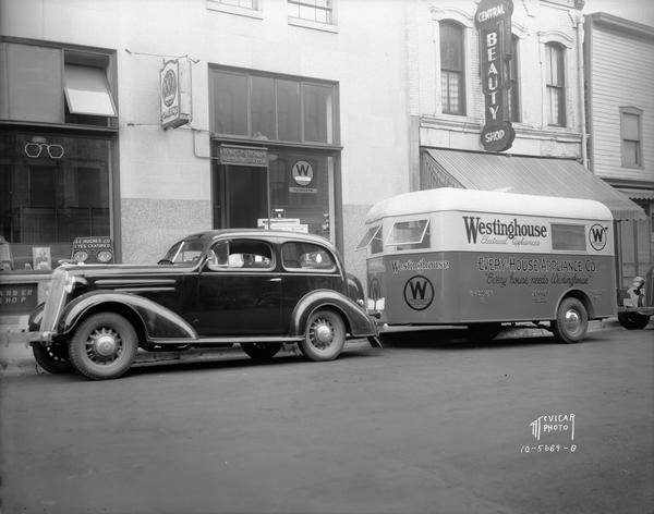 Parked automobile with Every-House Appliance Co. trailer-hitched, and advertising that reads: "Every House Needs Westinghouse," in front of the Westinghouse distributor at 114 E. Main Street.