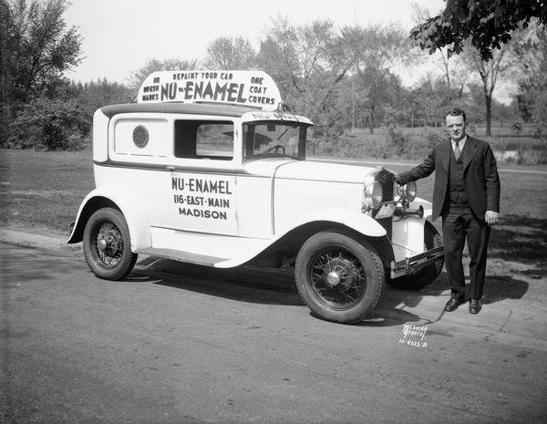 Man standing next to an automobile outfitted with signs advertising Nu-Enamel paint.