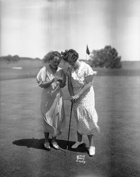 Two golfers, Miss Merle Nickles, and possibly Miss Marion Callahan, posing on the Nakoma Golf Course with putters.