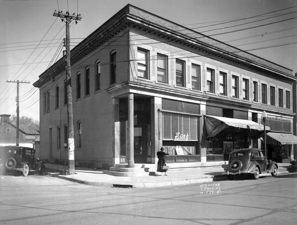 View from street towards a woman walking down the sidewalk in front of the Bank of Sun Prairie building, with Stoehr's variety store. There is a shoe store in the same block.