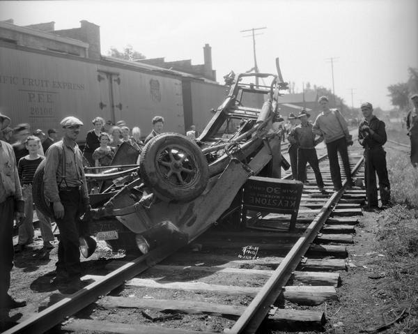 A crowd of people viewing the remains of a Keystone Fuel & Material Co. truck after it was crushed by a Milwaukee Road train, near the Brittingham Park crossing, in the Greenbush neighborhood. Thomas Haney, truck driver, was seriously injured. Two railroad cars are in the background.