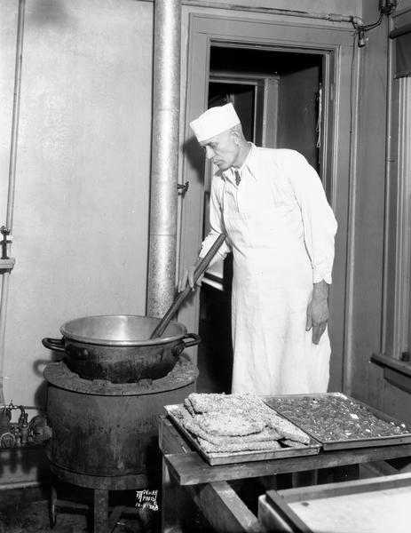 John Karch stirring a hot pot of candy syrup on a stove, while trays of finished candy are cooling on the table.