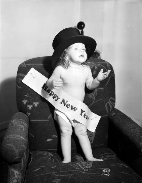 "Miss 1935," one-year-old Lois Ann Endres, daughter of Emil and Berniece Endres, 534 W. Mifflin Street, standing in an overstuffed chair wearing top hat and Happy New Year banner.