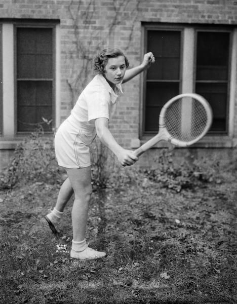 University of Wisconsin coed, Cecil McLaren, from Cincinnati, Ohio, co-champion in Western girls' doubles and finalist in National girls' tournament, demonstrates her backhand form with a tennis racket.