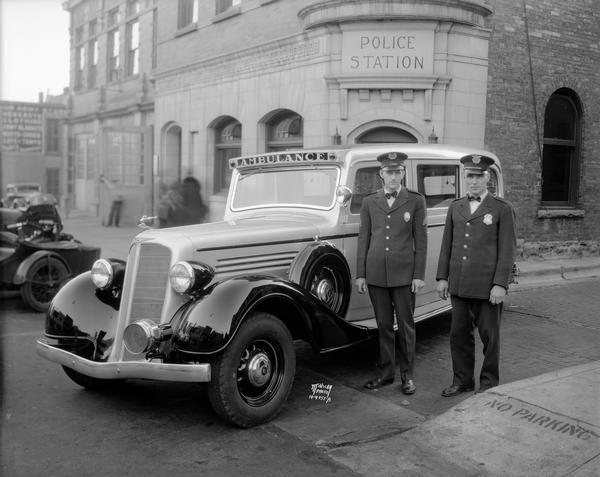 Two police officers are standing beside a new police ambulance parked in front of the Madison Police Station, 14-16 South Webster Street.