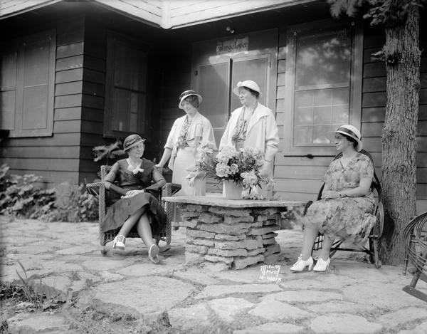 Women are relaxing on the stone terrace near the door to Bungalowen, the home of Professor Ray and Theo Owen in Frost Woods, 5805-7 Winnequah Road, during a University League garden party.