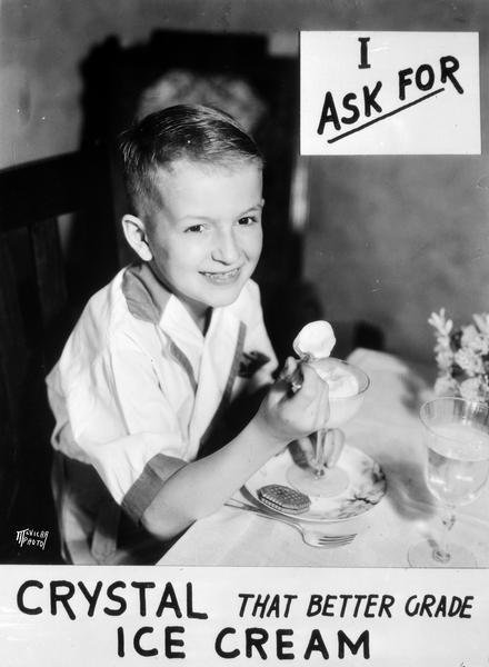 Richard McVicar, son of the photographer, sitting at a table and eating ice cream from a stemmed dish, under a sign advertising Crystal Ice Cream that reads: "I ask for Crystal, that better grade Ice Cream."
